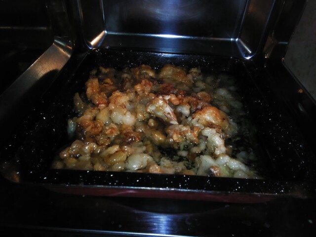 Picture showing a tray full of more than half cooked mutton fat pieces. They are browish in color and are partially immersed in fluid (fat+water+impurities)  that has seeped out.